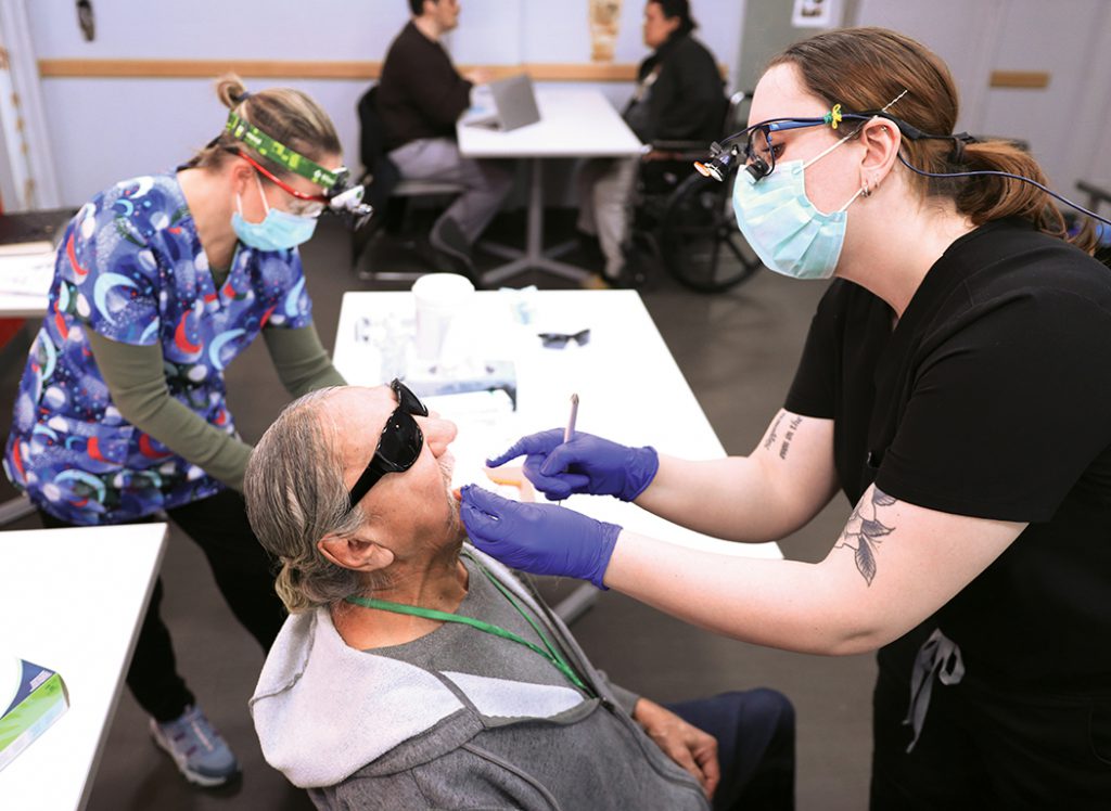 Oral health community liaisons Lezah Evan and Stacey Urban assess the oral health of Wayne, a resident at the Bell Hotel.