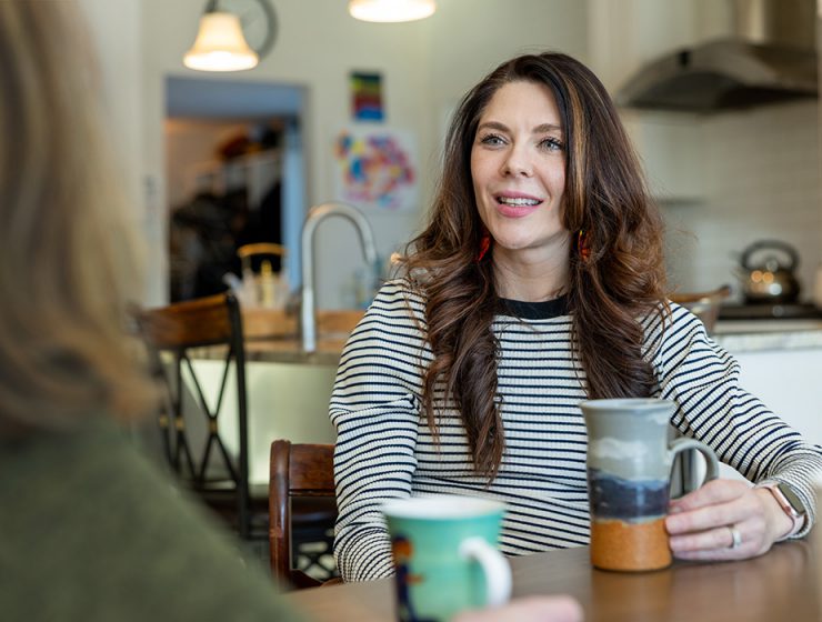 Vanessa Van Bewer speaks with another woman over coffee at a kitchen tabele.
