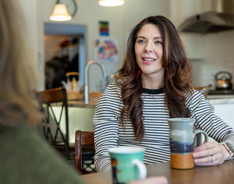 Vanessa Van Bewer speaks with another woman over coffee at a kitchen tabele.