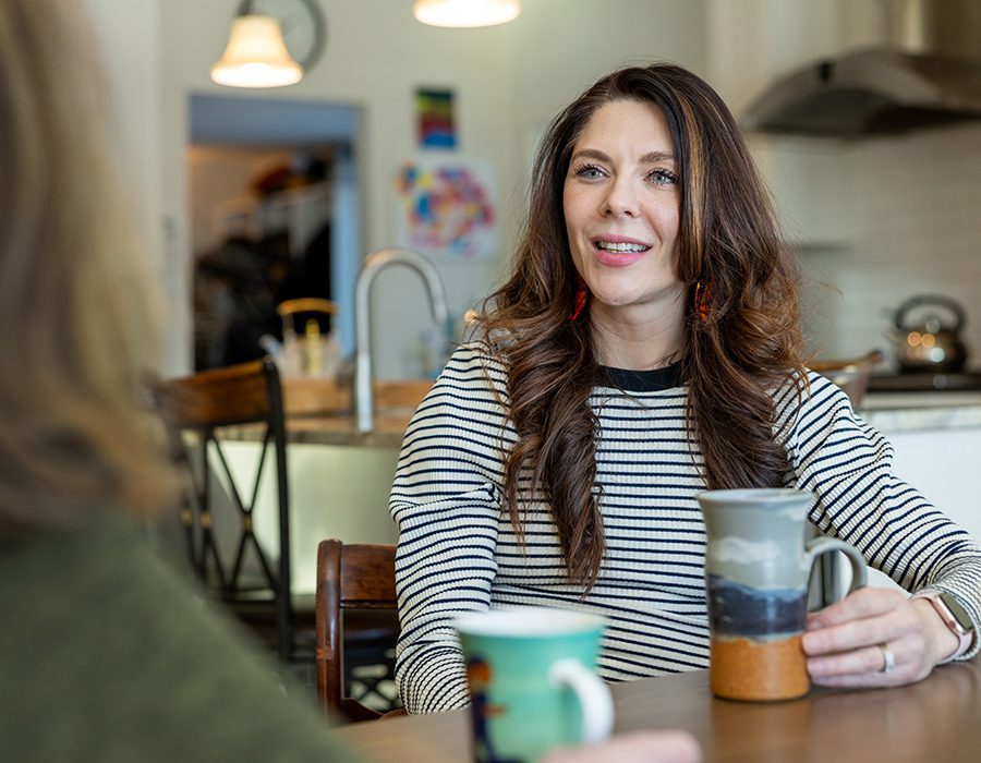 Vanessa Van Bewer speaks with another woman over coffee at a kitchen tabele.